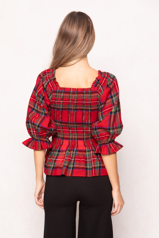 woman wearing a red plaid top with black pants and heels on a white backdrop 