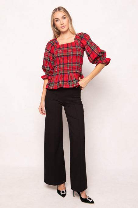 woman wearing a red plaid top with black pants and heels on a white backdrop 
