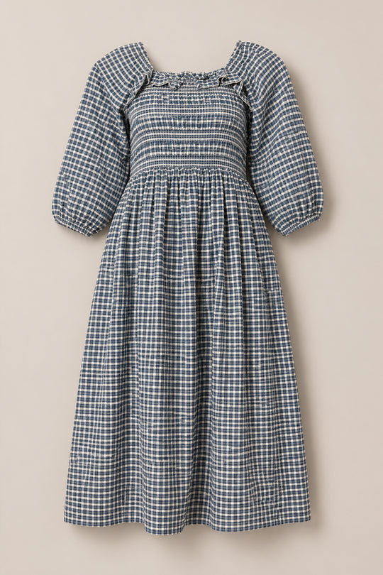 The Mae 3/4 Sleeves Dress in Prussian Blue Plaid by Ivy City Co features a blue and white plaid pattern, puffed 3/4 sleeves, a square neckline, and a smocked fitted bodice. With its gathered skirt that flows to mid-calf, this dress offers a comfortable, maternity-friendly silhouette. Displayed against a plain light background.