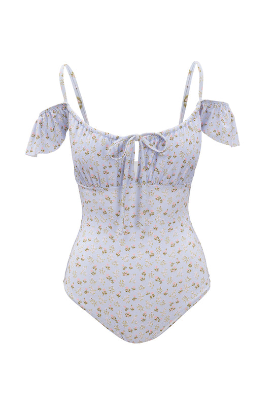 The Maise One Piece by Ivy City Co features a blue ditsy floral print with small yellow blooms, off-shoulder ruffled sleeves, and a front tie at the bust. This stylish swimsuit is shown on a white background.