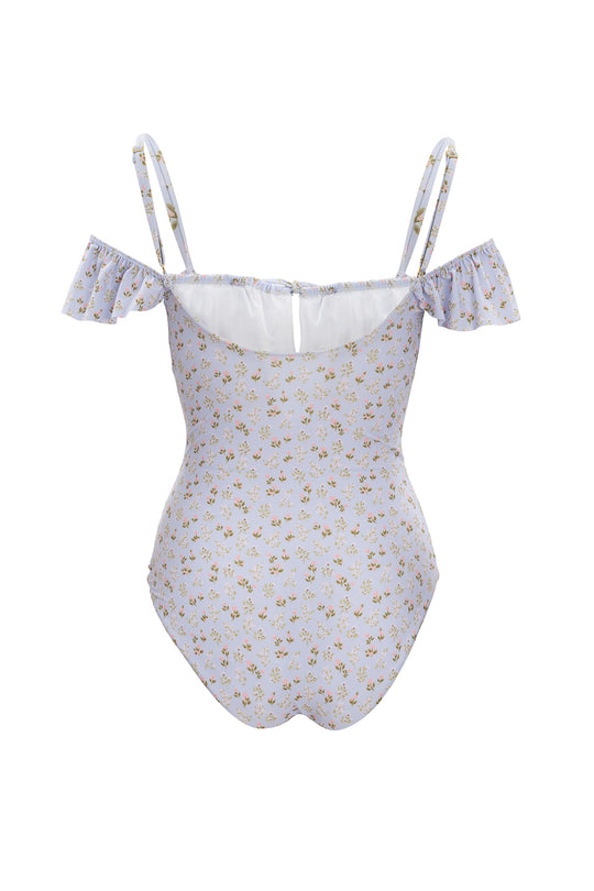 The Maise One Piece in Blue Ditsy Floral by Ivy City Co features thin shoulder straps, off-the-shoulder ruffled sleeves, and a small floral pattern. This swimsuit is displayed from the back.