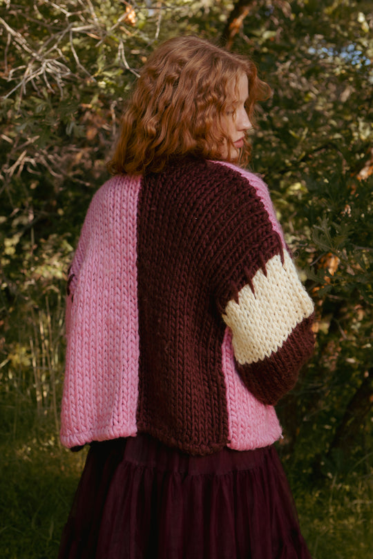 Person wearing a colorful knitted cardigan with a heart pattern in an outdoor setting.