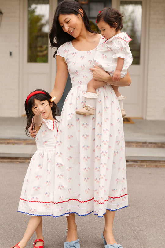 A woman and two children stand outside in matching Ivy City Co Marlow Cap Sleeve Dresses in Star Spangled, featuring white fabric with red and blue accents perfect for the Fourth of July.