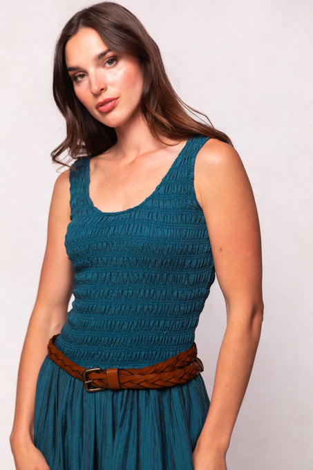 Woman wearing a teal dress with a brown belt against a light background