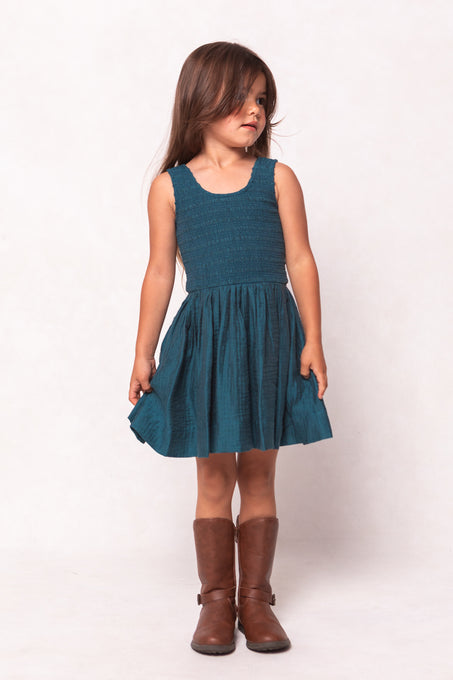 Young girl wearing a teal dress and brown boots on a white background