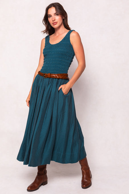 Woman wearing a teal dress with a brown belt and boots on a white background