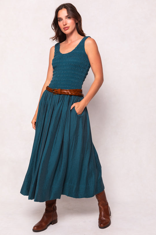 Woman wearing a teal dress with a brown belt and boots on a white background