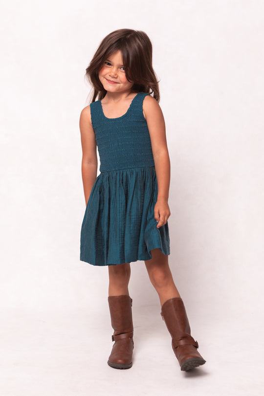 Young girl wearing a teal dress and brown boots on a white background