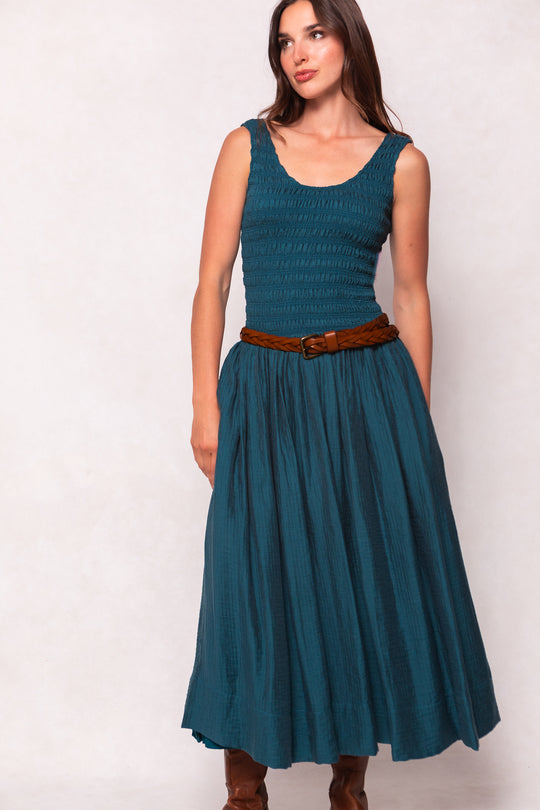 Woman wearing a teal dress with a brown belt against a white background