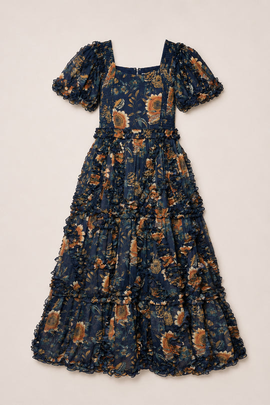 The Marseille Dress in Sunflower Twilight by Ivy City Co is an ankle-length, flowy navy blue dress adorned with a yellow and green sunflower floral print. It features puffed short sleeves, a square neckline, a tiered skirt, and delicate ruffle details.