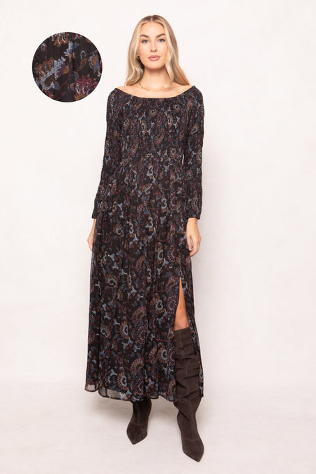 Woman wearing a long, dark floral-patterned dress with a slit on a white background.