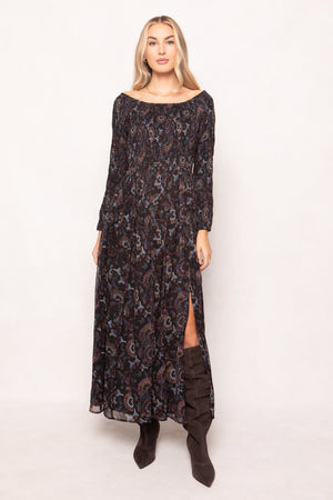 Woman wearing a long, dark patterned dress with brown boots on a white background
