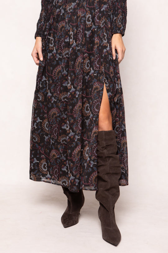 Person wearing a long patterned dress with a slit and brown knee-high boots on a white background