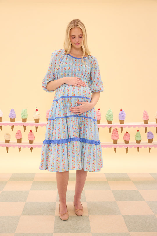 Pregnant woman wearing a floral dress with a checkered floor and ice cream cone display in the background.
