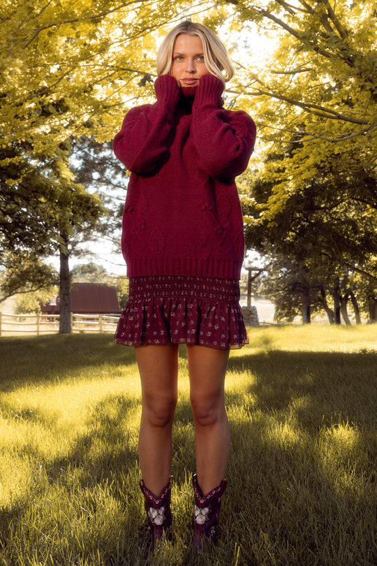 Woman in a red dress standing in a park with trees and grass.