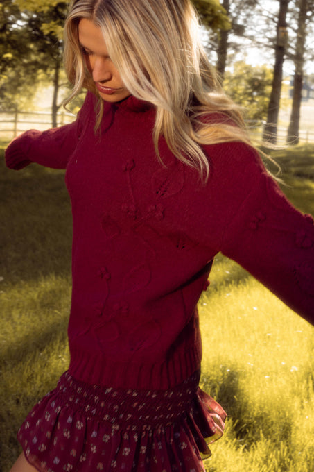 Woman wearing a red sweater and skirt in a grassy field with trees in the background