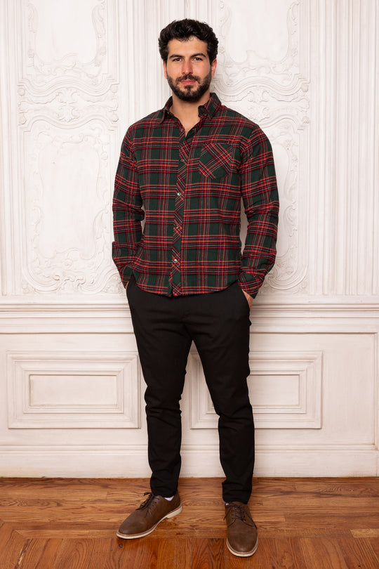 Man wearing a red and green plaid shirt against a white wall.
