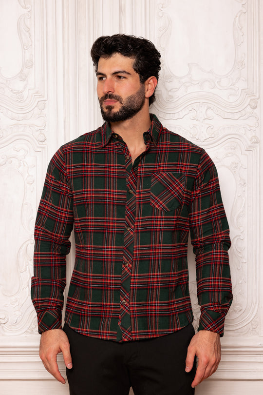 Man wearing a red and green plaid shirt against a white textured wall.