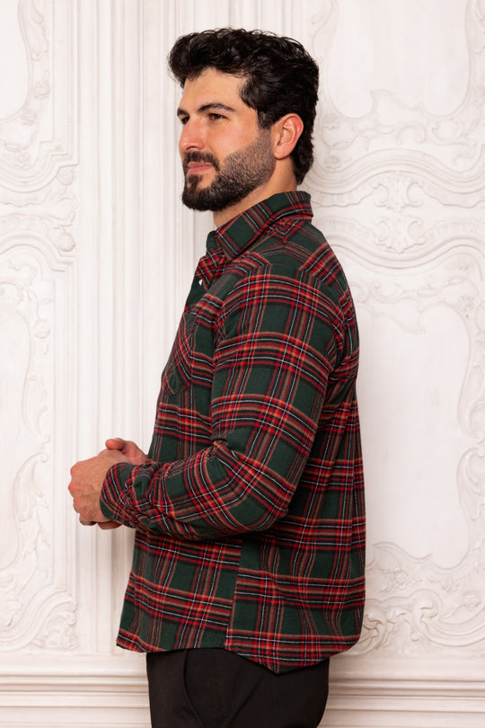 Man wearing a red and green plaid shirt against a white wall.