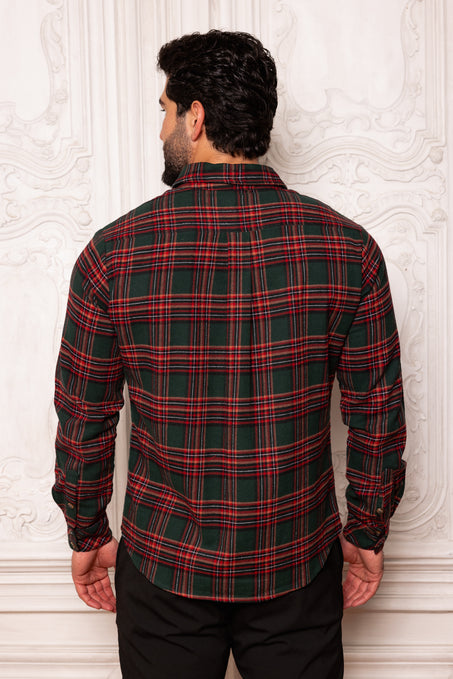 Man wearing a red and green plaid shirt against a white textured wall.