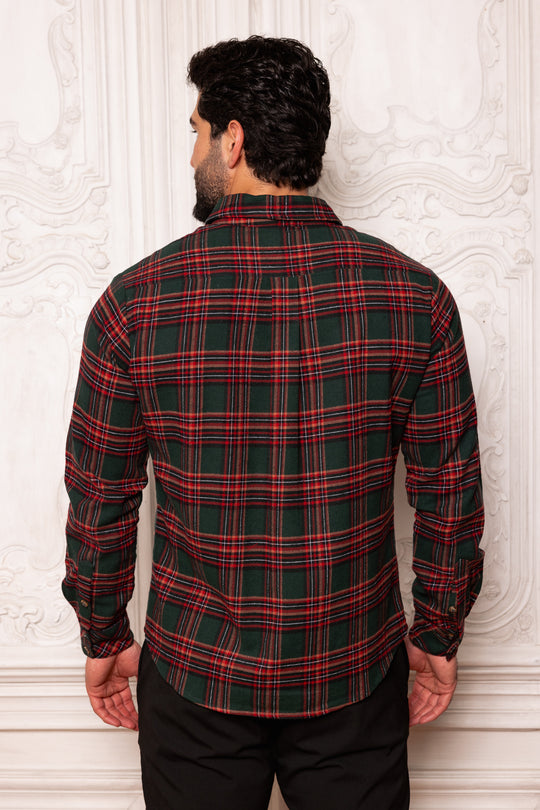 Man wearing a red and green plaid shirt against a white textured wall.