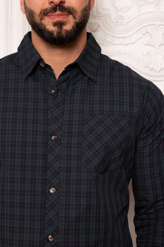 Man wearing a dark plaid shirt against a textured white wall