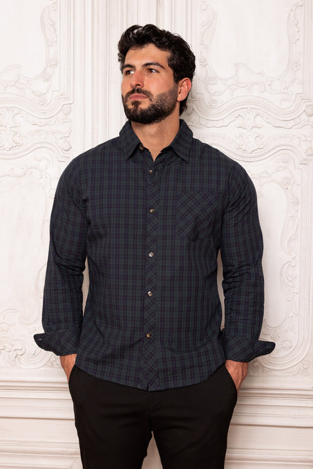 Man wearing a dark plaid shirt against a textured white wall
