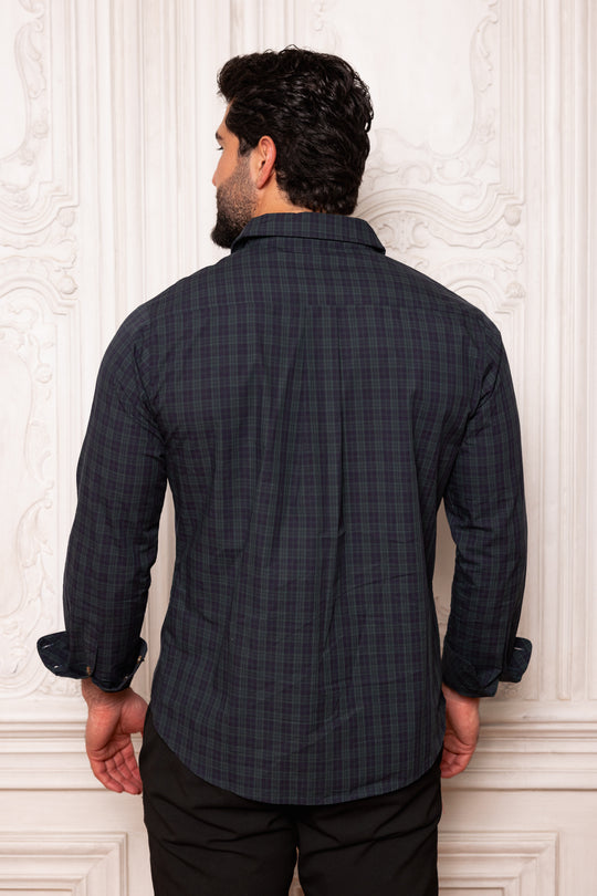 Man wearing a dark checkered shirt against a decorative white wall.