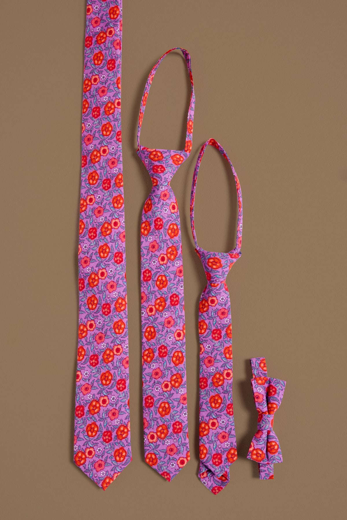 Three Ties in Thistle Flower Poppy Woodblock by Ivy City Co and one matching bow tie, all with a vibrant red and purple floral pattern, are arranged vertically on a brown background—perfect for family or mom and me sets.
