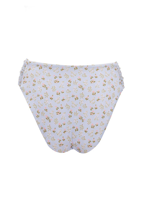 The Ivy City Co Mid Rise Ruched Bottom in Blue Ditsy Floral features cheeky coverage and delicate ruffled side trim, displayed from the back on a white background.