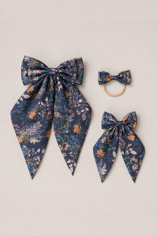 Three navy blue floral-patterned hair bows from Ivy City Co’s Hair Bows in Midnight Autumn Bouquet collection are beautifully displayed on a neutral background, featuring a large bow with tails, a smaller bow on a hair tie, and a medium-sized bow with tails.