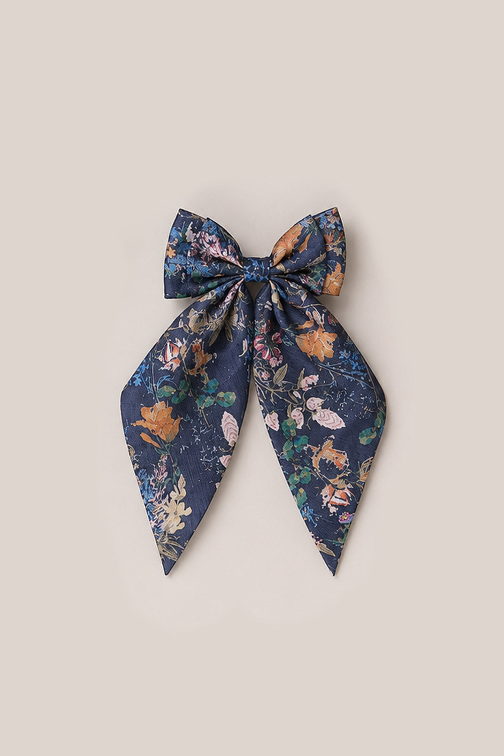 Discover the Hair Bows in Midnight Autumn Bouquet by Ivy City Co—a large fabric hair bow with long tails, adorned with a vibrant floral print against a dark blue background. Displayed on a plain beige surface, this charming accessory beautifully captures Ivy City Co’s signature elegance.