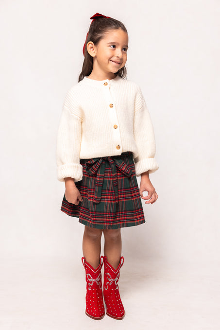 Young girl wearing a white sweater, plaid skirt, and red boots on a white background