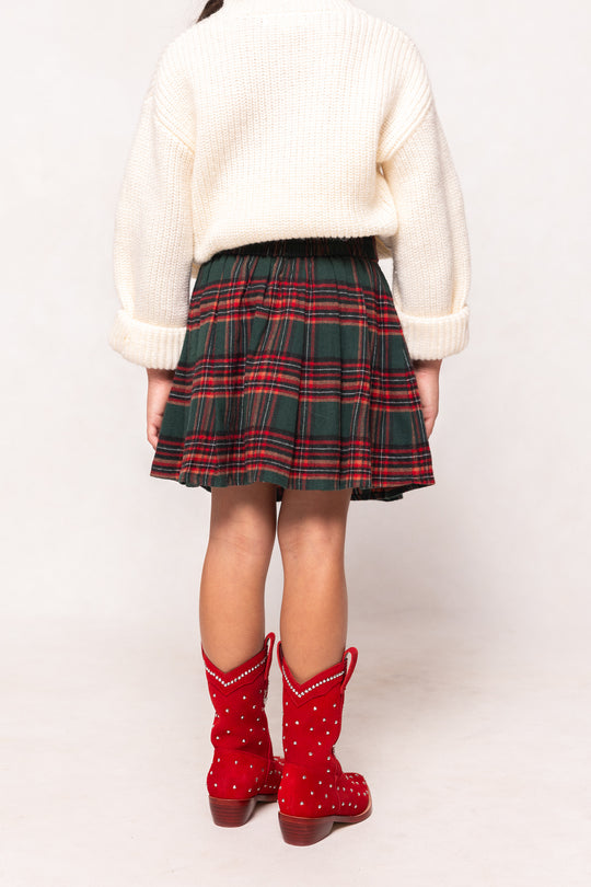 Person wearing a white sweater, plaid skirt, and red boots on a white background
