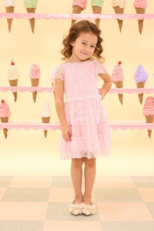 Young girl in a pink dress standing in front of ice cream cone decorations on a checkered floor.