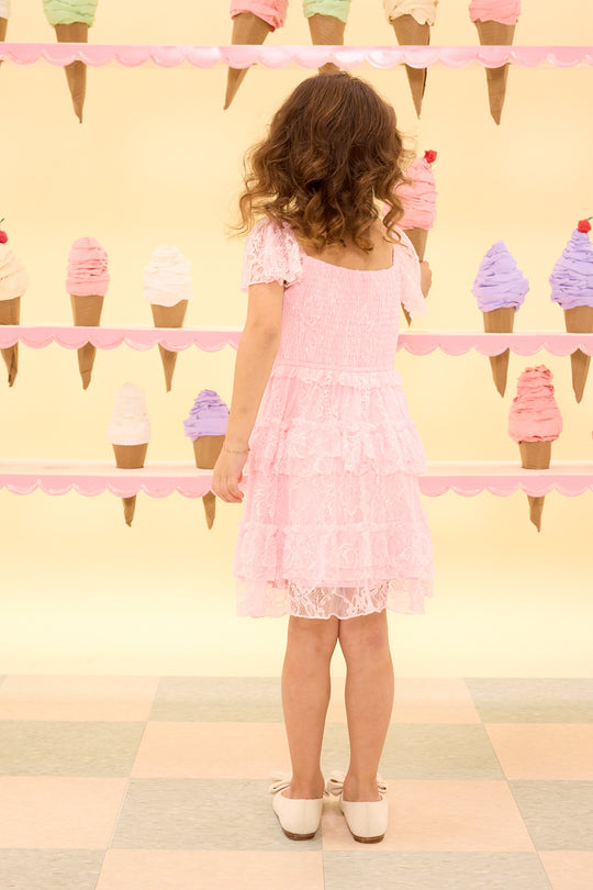 Young girl in a pink dress standing in front of a wall with ice cream cone decorations.