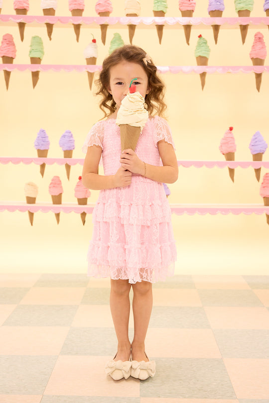 Young girl in a pink dress holding an ice cream cone in front of a wall with ice cream cone decorations.