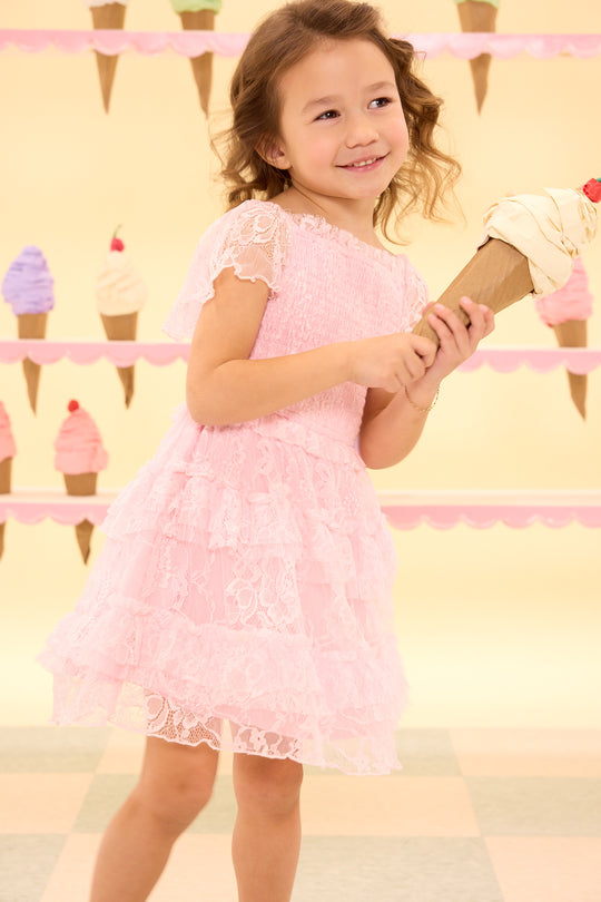 Young girl in a pink dress holding a toy ice cream cone with a pastel ice cream cone background.