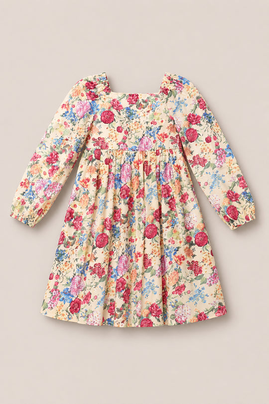 The Ivy City Co Mini Adelpha Dress in Autumn Amity Floral features long sleeves with charming balloon details, a square neckline, smocked bodice, and a colorful floral print on a light beige background, shown laid flat against a neutral surface.