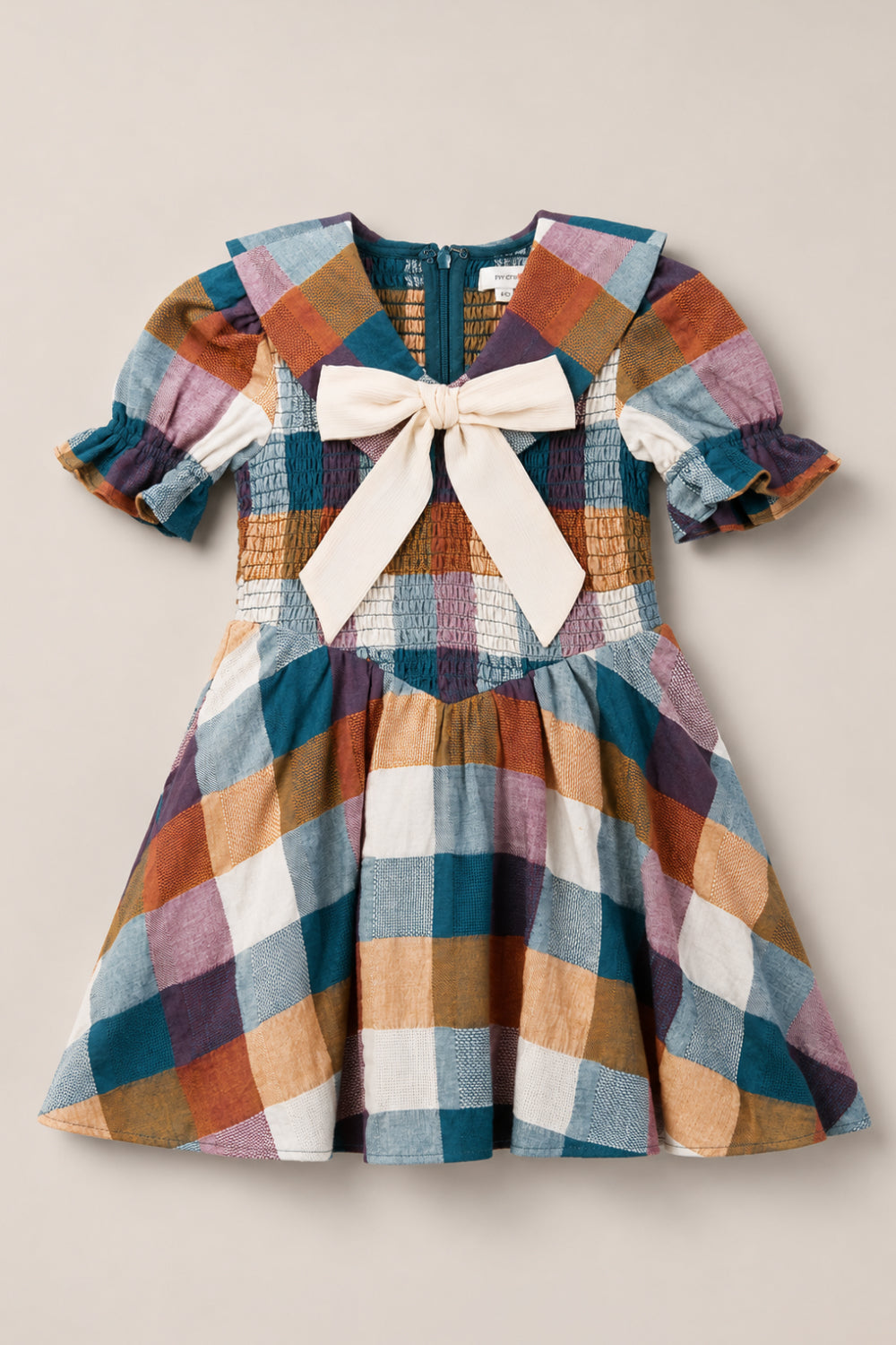 The Mini Alice Dress in Maize Gingham by Ivy City Co showcases a delightful plaid pattern in blue, white, mustard, and mauve checks. Featuring puff sleeves, a smocked bodice, sailor collar, back zipper, and a large cream bow on the front, this dress perfectly combines classic elegance with playful details.