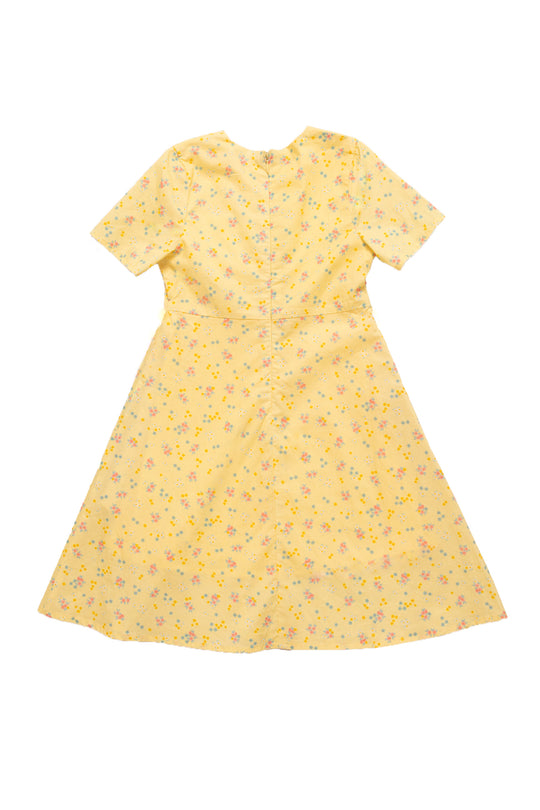 The Ivy City Co Mini Allie Dress in Yellow Floral is a girls’ cotton dress with short sleeves, flared skirt, and multicolored floral print, shown flat on a white background.