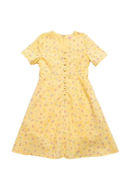 The Mini Allie Dress in Yellow Floral by Ivy City Co is a girls’ short-sleeved, knee-length cotton dress with a V-neckline, front buttons, and pastel floral print, displayed flat on a white background.