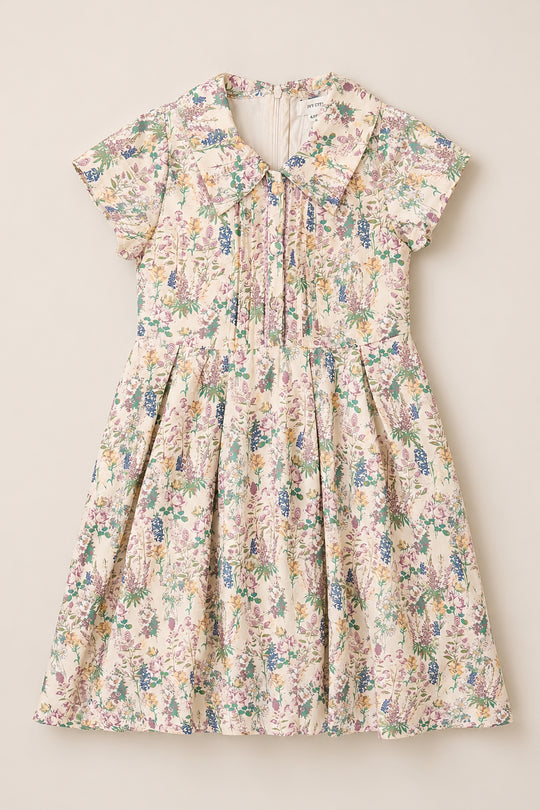 The Mini Amber Dress in Autumn Bouquet by Ivy City Co is a short-sleeved, children's midi-length dress featuring a floral print, pleated front, and Peter Pan collar—crafted from soft viscose and shown laid flat on a neutral background.