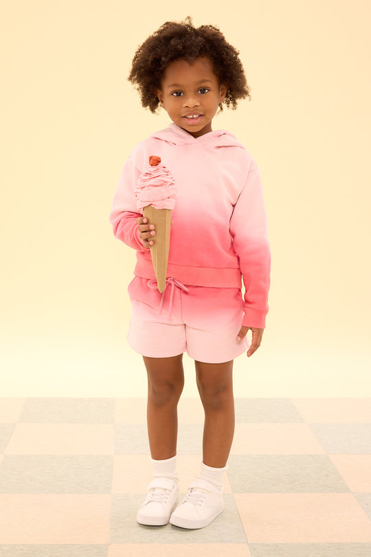Child wearing a pink and white gradient hoodie and shorts, holding a ice cream cone on a light background