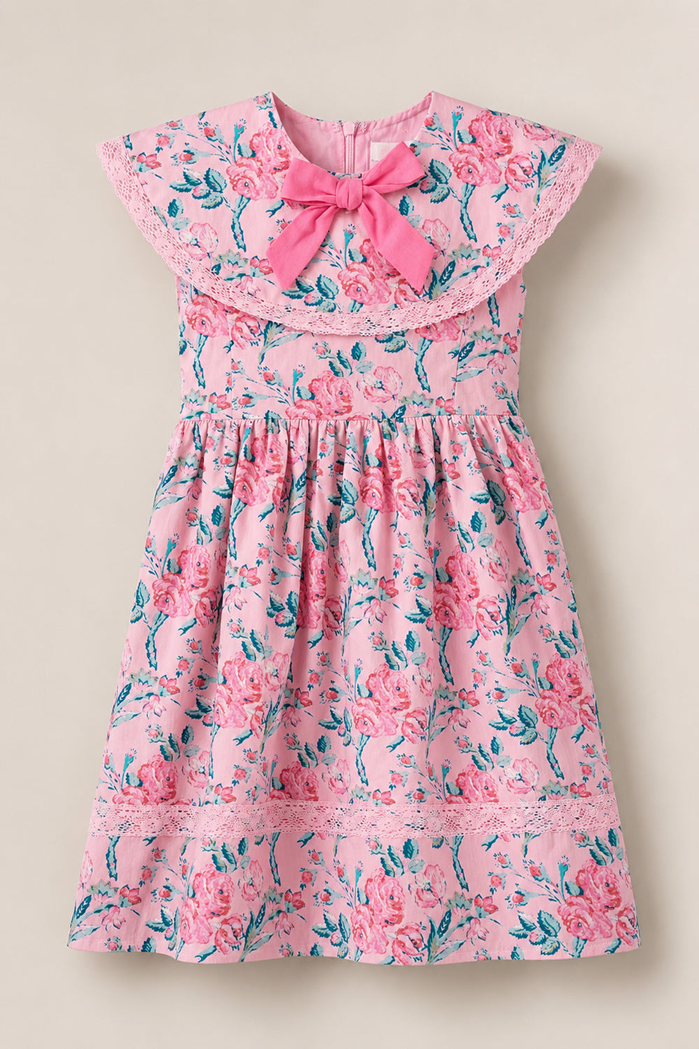 The Ivy City Co Mini Aster Dress in Pink Sketched Flower is a charming girls’ dress with a lace-trimmed collar, large pink bow, and a gathered skirt decorated with vibrant pink flowers and green leaves.