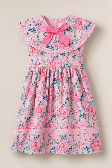 The Ivy City Co Mini Aster Dress in Pink Sketched Flower is a charming girls’ dress with a lace-trimmed collar, large pink bow, and a gathered skirt decorated with vibrant pink flowers and green leaves.