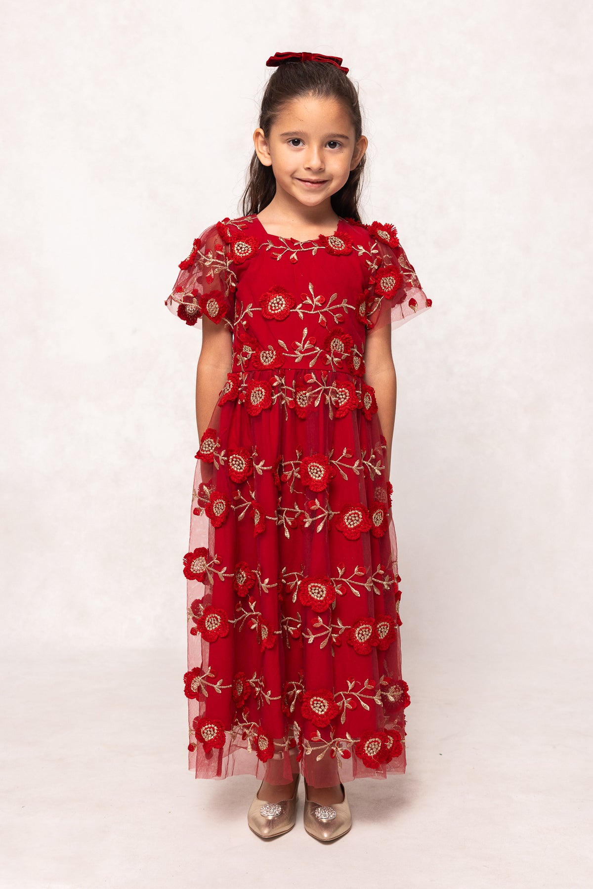 Young girl wearing a red dress with floral patterns on a white background
