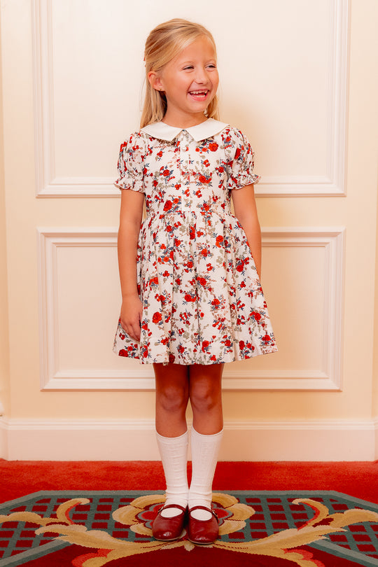 little girl in a white floral dress standing against a white wall