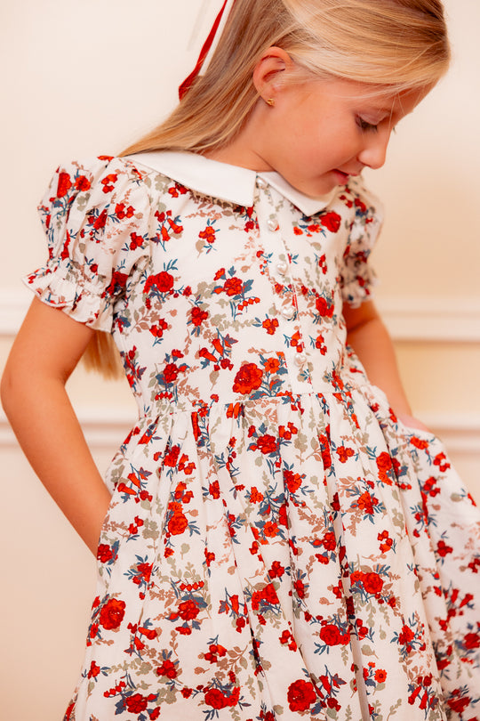 close up of a little girl in a white floral dress standing against a white wall