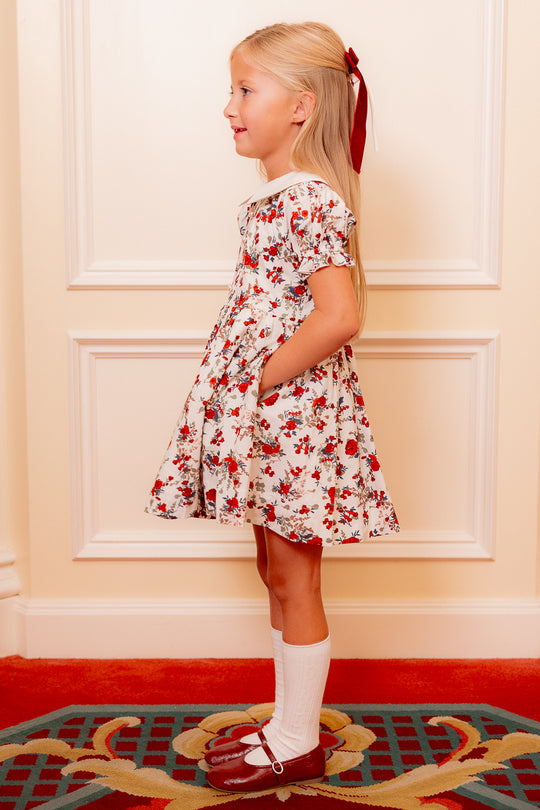 little girl in a white floral dress standing against a white wall